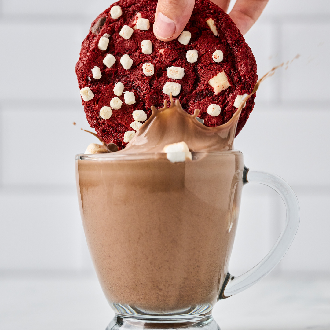 GREAT AMERICAN COOKIES A red velvet cookie being dipped in hot chocolate
